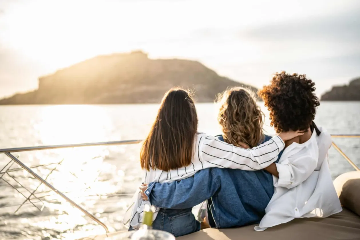 Young women embracing and looking away enjoying sunset on a yacht trip